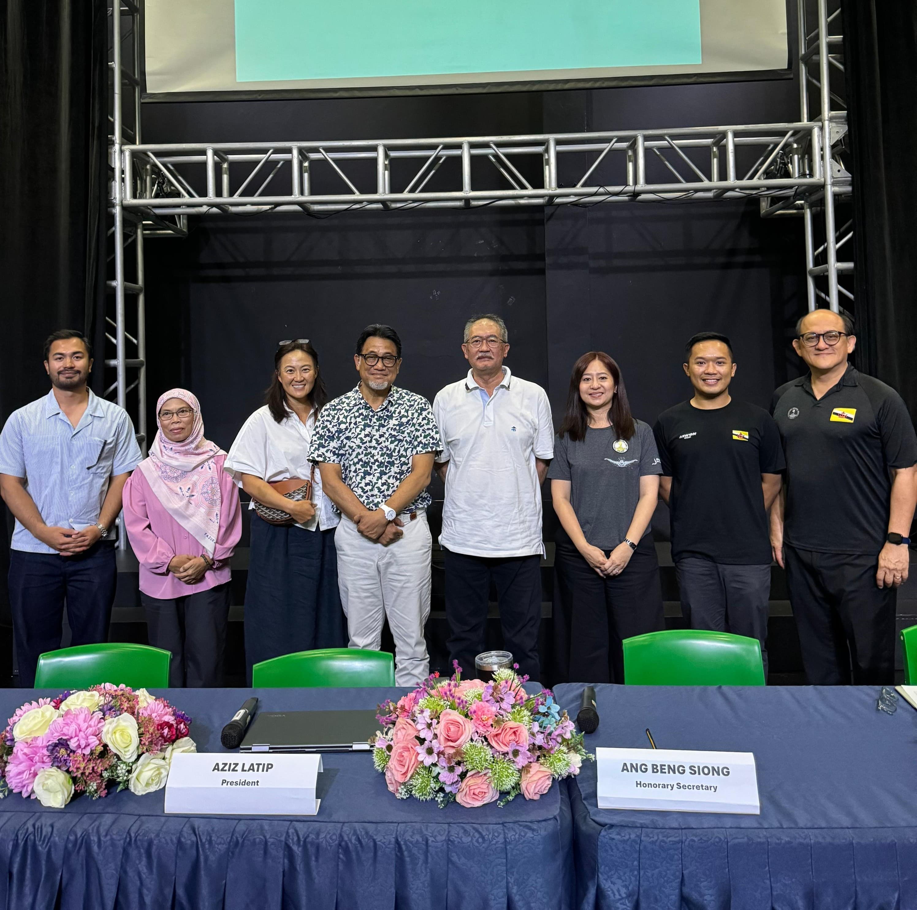 Brunei Aquatics Executive Committee, seven members standing behind a table with name placards, plus the Honorary Secretary.